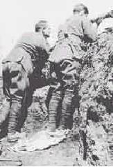 Two soldiers in uniform with backs to the camera, looking out of a trench