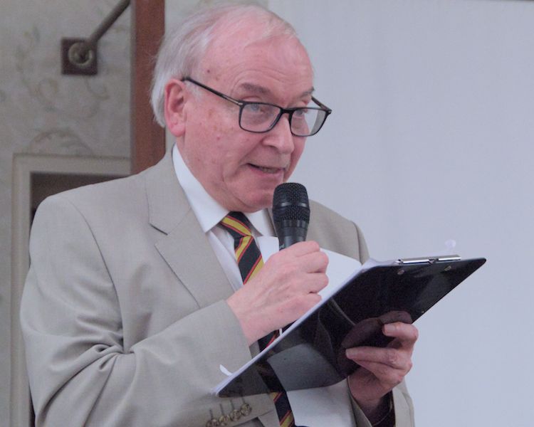 Richard Anderson holding a clipboard of notes and speaking into a microphone